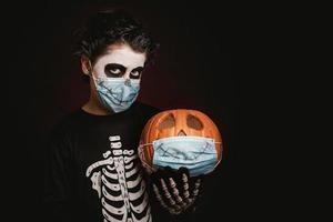 felice halloween.kid che indossa una maschera medica in un costume da scheletro con zucca di halloween foto