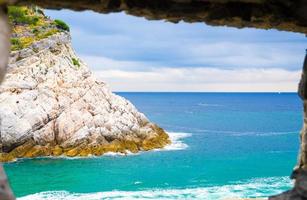 vista dell'acqua del mare ligure e della scogliera rocciosa dell'isola di Palmaria attraverso la finestra del muro di pietra di mattoni della città costiera di portovenere foto