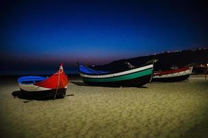 portogallo, spiaggia di nazare, barche di legno colorate sulla spiaggia di notte, vista panoramica della città di nazare foto