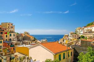 vista dall'alto di tetti di tegole arancioni di case multicolori con balconi e persiane di riomaggiore tipico villaggio di pescatori parco nazionale delle cinque terre, orizzonte mare ligure, liguria, italia foto