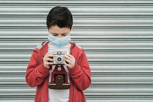 bambino con maschera medica scatta foto con la sua fotocamera