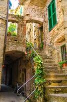 tipico piccolo cortile con edifici in pietra case, scale, persiane e vasi di fiori nel villaggio di corniglia foto