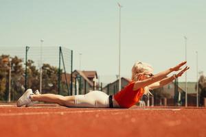 la giovane bionda scuote i muscoli addominali su un tappetino sportivo per strada foto