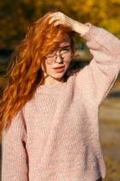 ritratti di un'affascinante ragazza dai capelli rossi con occhiali e viso carino. ragazza in posa nel parco autunnale con un maglione e una gonna color corallo. la ragazza ha un umore meraviglioso foto