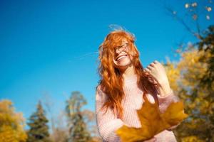 ritratti di un'affascinante ragazza dai capelli rossi con un viso carino. ragazza in posa nel parco autunnale con un maglione e una gonna color corallo. la ragazza ha un umore meraviglioso foto