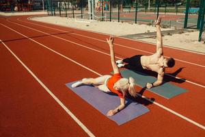 giovane coppia che fa sport nello stadio sdraiato su materassini da yoga foto