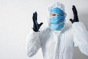 un uomo spaventato in tuta protettiva appeso con maschere mediche contro un muro bianco. gli orrori dell'epidemia, il pericolo del coronavirus, lo scienziato descrive sorpresa e disperazione foto