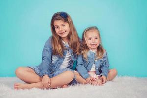 sorelle sorridenti che si siedono sul pavimento su fondo blu foto