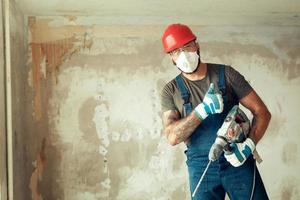 un costruttore con un perforatore pone sullo sfondo di un muro con spazio vuoto dal testo il costruttore è vestito con una tuta protettiva e un casco foto