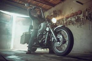 bell'uomo brutale con la barba seduto su una moto nel suo garage foto