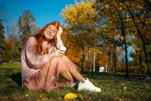 ritratti di un'affascinante ragazza dai capelli rossi con occhiali e un bel viso. ragazza in posa nel parco autunnale con un maglione e una gonna color corallo. foto