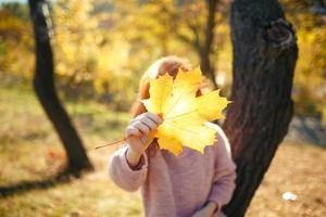 ritratti di un'affascinante ragazza dai capelli rossi con un viso carino. ragazza in posa nel parco autunnale con un maglione e una gonna color corallo. nelle mani di una ragazza una foglia gialla foto