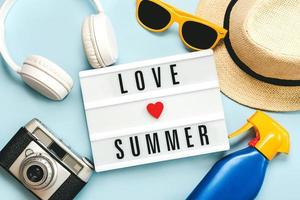 vacanze estive concept.lightbox con il testo amore estate accanto a occhiali da sole, cappello, bottiglia di plastica di crema solare, cuffie e macchina fotografica vintage foto