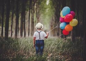 vista posteriore del bambino premuroso con palloncini nella foresta foto