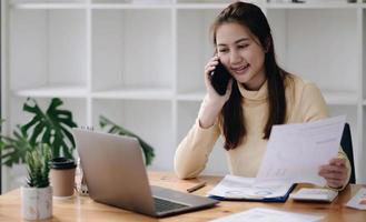 donna asiatica d'affari che utilizza smartphone per fare finanza matematica sulla scrivania di legno in ufficio, tasse, contabilità, concetto finanziario foto