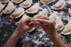 donna scolpisce gnocchi con patate fatte a mano su sfondo nero. ripresa dall'angolo superiore. cucina popolare ucraina. foto