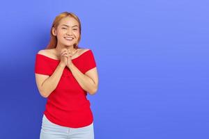 sorridente bella donna asiatica in abito rosso strofinando le mani e guardando fiducioso isolato su sfondo viola foto