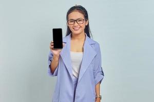 Ritratto di giovane donna asiatica sorridente che mostra il telefono cellulare con schermo vuoto isolato su sfondo bianco foto
