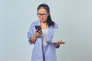 ritratto di giovane donna asiatica arrabbiata che guarda il messaggio sullo smartphone e tiene in mano un laptop, sapendo che il lavoro annullato è isolato su sfondo bianco foto