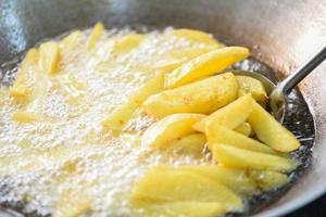 cucinare patatine fritte o friggere patate in olio bollente per spicchi di patate, chiudere patate fritte in olio su padella foto