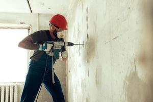 costruttore con perforatore pratica fori nel muro di cemento foto