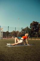 bella bionda che fa stretching sul prato di un campo da calcio foto