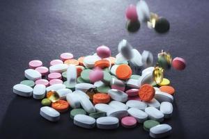 pillole mediche colorate, capsule o integratori per il trattamento e l'assistenza sanitaria su sfondo nero foto