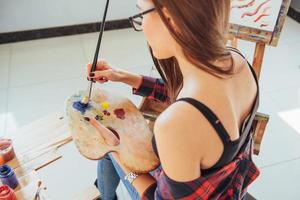 artista ragazza piuttosto carina dipinge su tela dipinto sul cavalletto foto