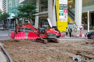 bangkok tailandia 7 febbraio 2022 - il lavoratore si siede e suona il telefono cellulare sul sedile del conducente della terna alla costruzione si siede con la strada sfocata e il paesaggio in backgroud foto