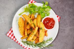 spicchi di patate su piatto bianco con coriandolo alle erbe di rosmarino e salsa di ketchup, cottura di patatine fritte o patate fritte foto