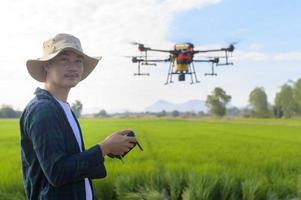 giovane agricoltore intelligente che controlla i droni che spruzzano fertilizzanti e pesticidi su terreni agricoli, innovazioni ad alta tecnologia e agricoltura intelligente foto