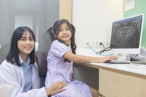 dentista femminile che spiega i raggi x dei denti a una bambina in clinica dentale, controllo dei denti e concetto di denti sani foto