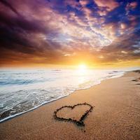 disegnando il cuore sulla sabbia gialla sul fantastico tramonto foto