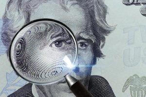 la banconota del dollaro sotto una lente d'ingrandimento viene ispezionata su sfondo bianco foto