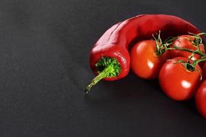 ramo di pomodori e peperoncino rosso, isolato su sfondo nero foto