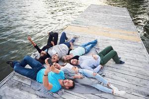 gruppo di bei giovani che fanno selfie sdraiati sul molo, i migliori amici di ragazze e ragazzi con il concetto di piacere creano la vita emotiva delle persone. foto