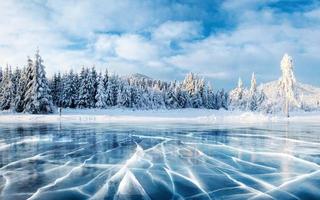 ghiaccio blu e crepe sulla superficie del ghiaccio. lago ghiacciato sotto un cielo blu in inverno. le colline dei pini. inverno. carpazi, ucraina, europa. foto