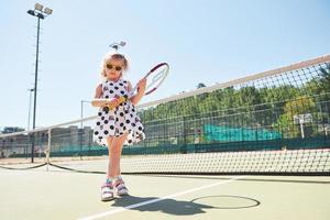 bambina sveglia che gioca a tennis sul campo da tennis all'esterno foto