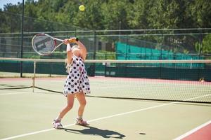 bambina sveglia che gioca a tennis sul campo da tennis all'esterno foto