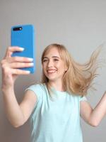 blogger elegante e bella donna bionda che fa selfie con il suo smartphone vicino alla finestra. tendenza, tecnologia, bellezza, concetto di moda foto