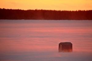 capanna di pesca sul ghiaccio sul lago ghiacciato al tramonto foto