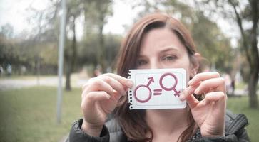 bella donna ispanica nel mezzo di un parco che tiene in mano un foglio con il messaggio di uguaglianza con le icone dell'uomo e della donna foto