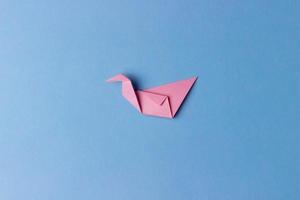 un uccello origami piegato da carta rosa su sfondo blu al centro della foto