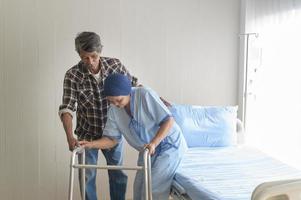uomo anziano che aiuta la donna malata di cancro che indossa una sciarpa per la testa con il deambulatore in ospedale, assistenza sanitaria e concetto medico foto