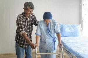 uomo anziano che aiuta la donna malata di cancro che indossa una sciarpa per la testa con il deambulatore in ospedale, assistenza sanitaria e concetto medico foto