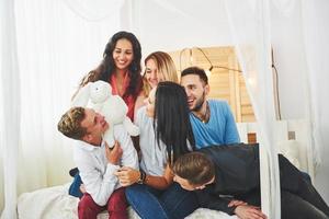 ritratto di gruppo di ragazzi e ragazze multietnici con abiti colorati alla moda che tengono un amico e posano su un muro di mattoni, persone in stile urbano che si divertono, concetti di gioventù e stile di vita foto