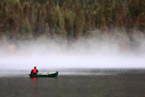 uomo in canoa vicino alla nebbia mattutina sul lago foto