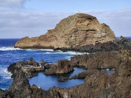 piscine naturali nel mezzo dell'oceano atlantico a porto moniz, isola di madeira, portogallo. fantastici periodi di vacanza. nuvole con il sole. oceano e onde che colpiscono le rocce. persone in acqua. foto