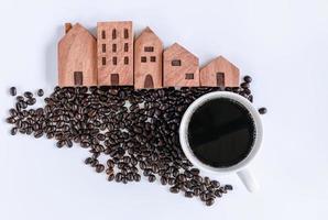 caffè fatto in casa e concetto di comunità di caffè, tazza di caffè e chicchi di caffè tostati con modello di casa in legno su sfondo bianco isolato. primo piano di sfondi di ingredienti per bevande caffè in grani. foto