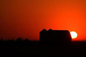 sole che tramonta dietro i granai di metallo del saskatchewan foto